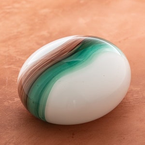 May include: A white glass paperweight with brown and green swirls.