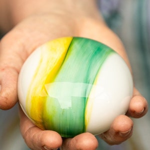 May include: A white sphere with yellow and green marbling. The sphere is smooth and glossy.