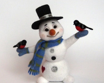 Könnte beinhalten: Ein weißer Schneemann mit einem schwarzen Zylinder, einem blau-grünen Schal und einem roten Herzen auf der Brust. Zwei kleine schwarze und rote Vögel sitzen auf den Armen des Schneemanns.