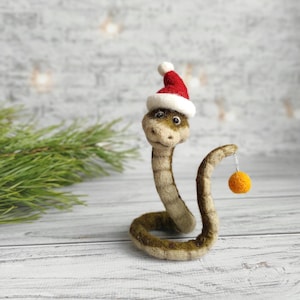 Op de afbeelding: Een vilt slang met een rood-witte kerstmanmuts en een gele ornament.