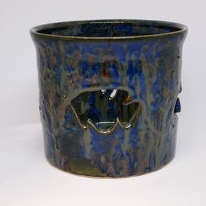 May include: A blue and green ceramic planter with a unique design. The planter has a textured surface and a cutout design.