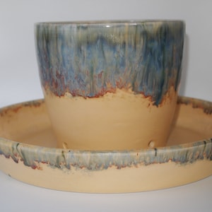 May include: A ceramic planter set with a blue and yellow glaze. The planter has drainage holes and a matching saucer.