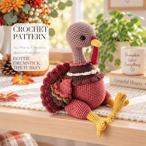 May include: A crochet turkey toy with a light brown head, a red wattle, a yellow beak, and a round body in shades of dark brown and rust red. The turkey has yellow feet and a multi-layered tail featuring scalloped edges in red, brown, and olive green.