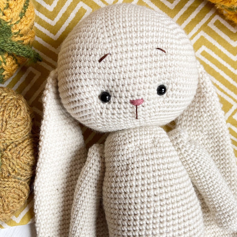 May include: A crocheted white bunny with long ears. The bunny has black eyes and a pink nose.