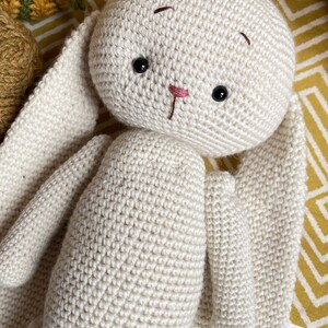 May include: A crocheted white bunny with long ears. The bunny has black eyes and a pink nose.
