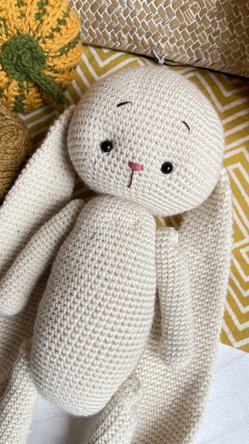 May include: A crocheted white bunny with long ears. The bunny has black eyes and a pink nose.