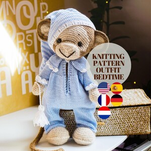 Op de afbeelding: Breipatroon voor een gehaakte aap die een blauwe pyjama en een witte slaapmuts draagt. Het patroon is beschikbaar in het Engels, Spaans, Frans, Duits en Nederlands. De aap zit op een gevlochten mand.