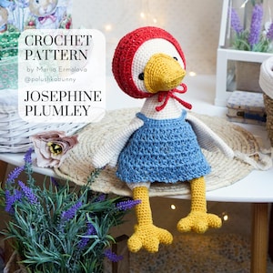 Puede incluir: Patrón de crochet para Josephine Plumley, una oca de crochet que lleva un gorro rojo con capucha y un vestido azul. El patrón es de Maria Ermolova, @polushkabunny.