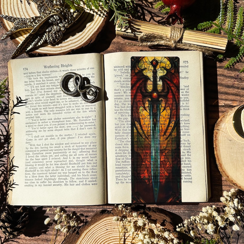 May include: A colourful bookmark featuring a sword with a blue blade and a red and gold hilt. The bookmark is surrounded by a stained glass-like design with intricate details and text.