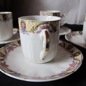 May include: Set of four white porcelain teacups and saucers with gold trim and floral designs. The cups have a fluted design and the saucers have a scalloped edge.
