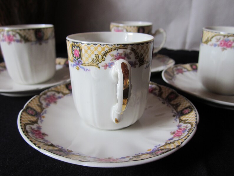May include: Set of four white porcelain teacups and saucers with gold trim and floral designs. The cups have a fluted design and the saucers have a scalloped edge.