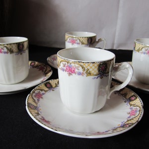 May include: Set of four white porcelain teacups and saucers with a floral pattern in shades of pink, yellow, and blue. The cups and saucers have a gold trim and a delicate floral design.