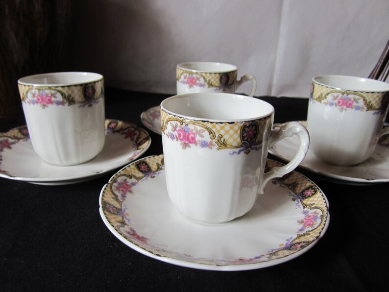 May include: Set of four white porcelain teacups and saucers with a floral pattern in shades of pink, yellow, and blue. The cups and saucers have a gold trim and a delicate floral design.