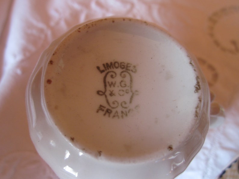 May include: Close-up of the base of a white porcelain teacup with a gold inscription that reads "LIMOGES W.G. & Co. FRANCE".