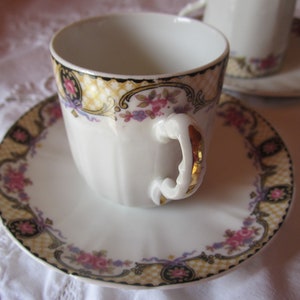May include: A white porcelain teacup and saucer with a gold trim and floral pattern. The cup has a decorative handle with gold accents.