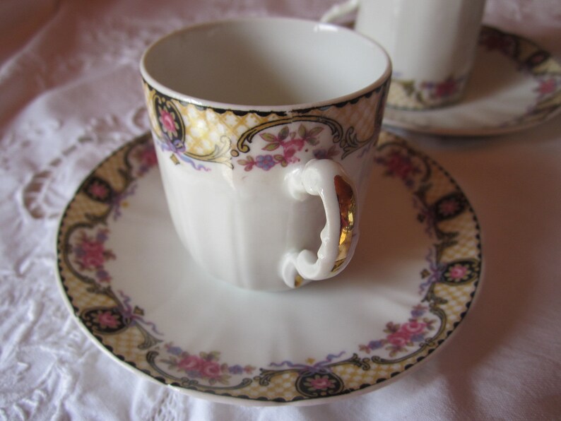 May include: A white porcelain teacup and saucer with a gold trim and floral pattern. The cup has a decorative handle with gold accents.
