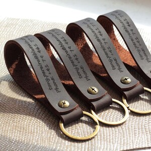May include: Four dark brown leather keyrings with gold-coloured rings. Each keyring has a loop with text and is secured with a brass screw. The text on each keyring reads: tony.persira@bluewind, Phone: +42 79 461 77.