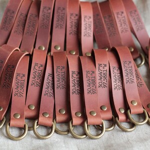 May include: Several brown leather keyrings with brass-coloured rings and rivets. Each keyring is engraved with the coordinates "30.4647°N 97.5881°W". The keyrings are fanned out, showing the engraved text.