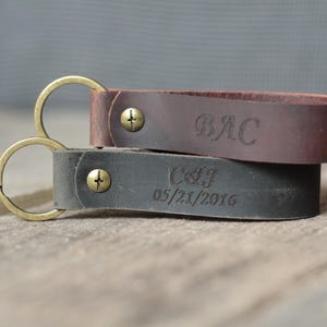 May include: Two leather keyrings with brass rings. One is dark brown with "BAC" engraved, the other is grey with "C&J 05/21/2016" engraved. Both have brass screws.