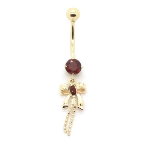 May include: Gold belly button ring with a red gemstone and a dangling bow with a chain.