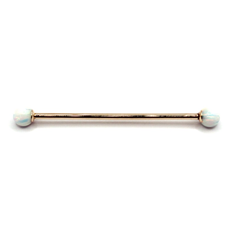 May include: Gold barbell with opal ends. The barbell is a straight piece of metal with rounded ends. The opal ends are white with a slight iridescent sheen.