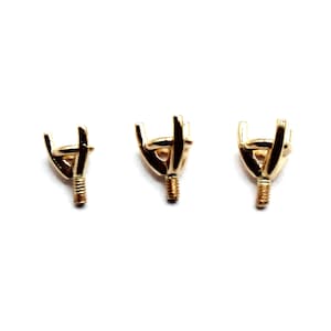 May include: Three gold-toned metal prongs for setting gemstones. The prongs are in different sizes, with the smallest on the left and the largest on the right.