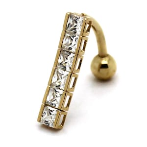 Può includere: Un piercing per l'ombelico color oro con un design a bilanciere curvo. L'anello presenta una barra dritta con cinque gemme quadrate e trasparenti. Una piccola sfera dorata si trova all'estremità della parte curva.
