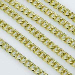 Könnte beinhalten: Nahaufnahme einer goldenen Kettenkette mit einem strukturierten, diamantgeschliffenen Design. Die Kette wird in mehreren Reihen gezeigt, wodurch die komplizierten Details des Designs hervorgehoben werden.