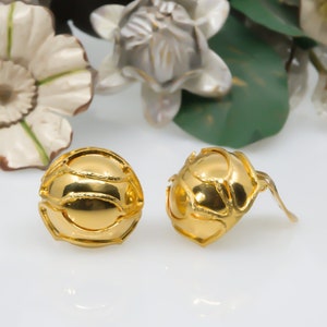 May include: A pair of gold-toned earrings with a textured, spherical design. The earrings have a post and a small, curved back.