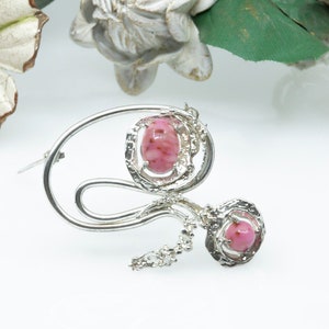May include: A silver brooch with a swirling design and two pink stones.