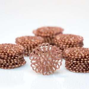 Puede incluir: Una pila de encaje de metal de color oro rosa, con un encaje colocado plano frente a la pila.