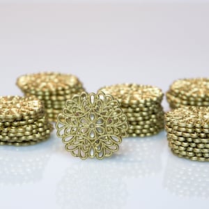Könnte beinhalten: Ein Stapel goldfarbener Metallszierstücke mit einem zarten Blumenmuster. Die Zierstücke sind in einer Reihe auf einer weißen Oberfläche angeordnet.