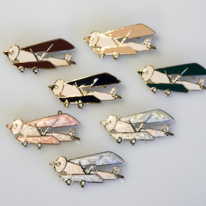 Könnte beinhalten: Satz von zehn Flugzeug-Anstecknadeln aus Emaille in verschiedenen Farben, darunter Schwarz, Weiß, Grün, Braun und Rosa. Jede Anstecknadel zeigt ein kleines, detailliertes Flugzeugdesign.