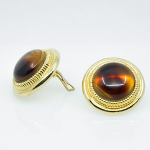 May include: A pair of gold tone clip-on earrings with brown, round, cabochon stones.