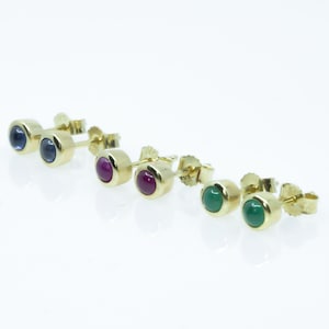 Könnte beinhalten: Drei Paar goldene Ohrstecker mit verschiedenen Edelsteinen. Das erste Paar hat blaue Edelsteine, das zweite Paar hat rote Edelsteine und das dritte Paar hat grüne Edelsteine.