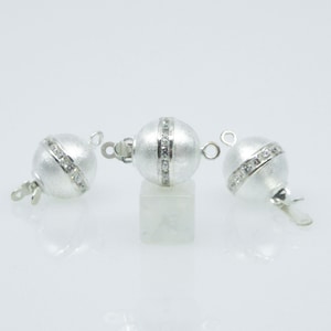 Könnte beinhalten: Drei silberne Kugelverschlüsse mit einer Reihe klarer Kristalle um die Mitte jeder Kugel.