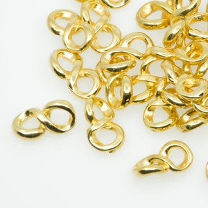 Puede incluir: Un montón de conectores de símbolo de infinito de metal dorado. Estos conectores se utilizan para la fabricación de joyas y la artesanía.