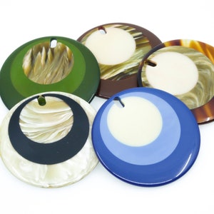 May include: Five round, decorative, colorful, patterned, resin ornaments with a hole in the center. The ornaments are in shades of green, brown, blue, white, and black.
