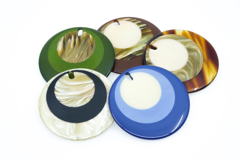 May include: Five round, decorative, colorful, patterned, resin ornaments with a hole in the center. The ornaments are in shades of green, brown, blue, white, and black.