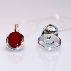 May include: A silver ring and pendant set with a red carnelian stone. The ring is open back and the pendant has a silver chain.