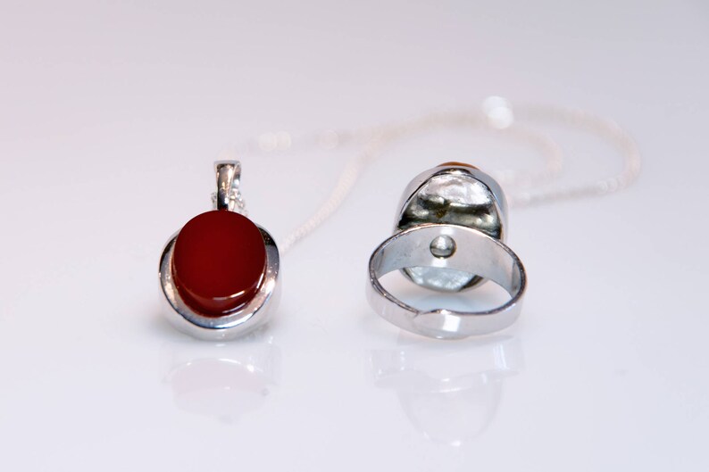 May include: A silver ring and pendant set with a red carnelian stone. The ring is open back and the pendant has a silver chain.
