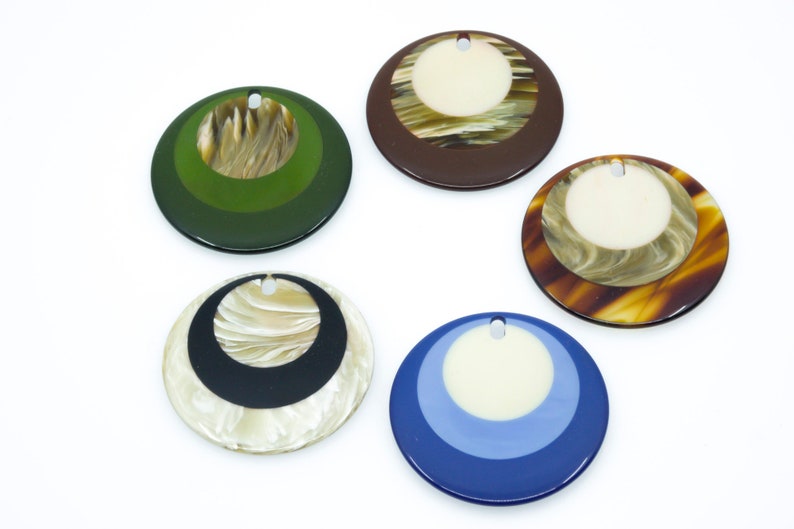 May include: Five round, decorative, multi-colored, resin pendants with a hole at the top for hanging. The pendants have a concentric circle design with a white center circle.