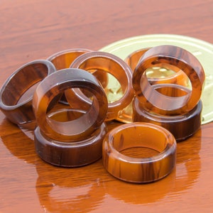 May include: A collection of brown and amber rings, possibly for napkin holders, arranged on a reflective wooden surface. The rings have a marbled appearance, with variations in colour and pattern. A gold-coloured, circular object is in the background.