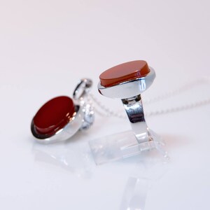 May include: A silver ring and pendant set with red carnelian stones. The ring has a simple band and the pendant is on a silver chain.
