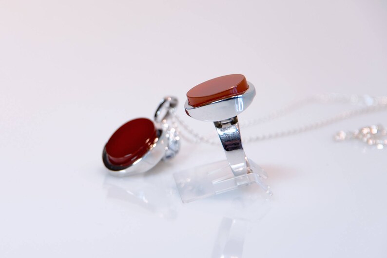 May include: A silver ring and pendant set with red carnelian stones. The ring has a simple band and the pendant is on a silver chain.