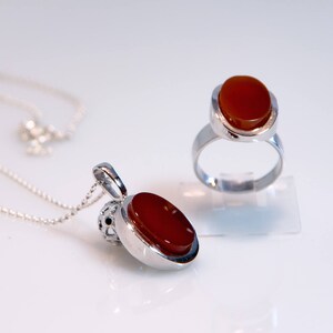 May include: A silver necklace with a red carnelian pendant and a silver ring with a red carnelian stone.