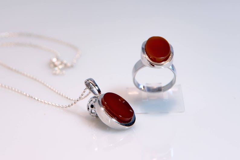May include: A silver necklace with a red carnelian pendant and a silver ring with a red carnelian stone.
