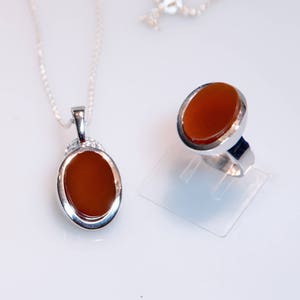 May include: A silver necklace and ring set with oval-shaped carnelian stones. The stones are a deep orange color and are set in silver.