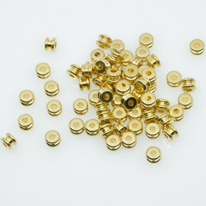 May include: A pile of gold-coloured metal beads, some are round and some are cylindrical.