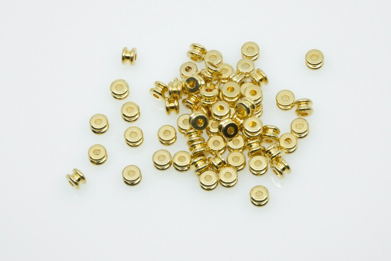 May include: A pile of gold-coloured metal beads, some are round and some are cylindrical.